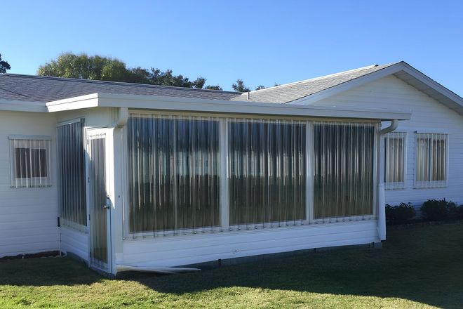 A white house with a sunroom featuring vertical, translucent vinyl weather curtains and a door on the side.