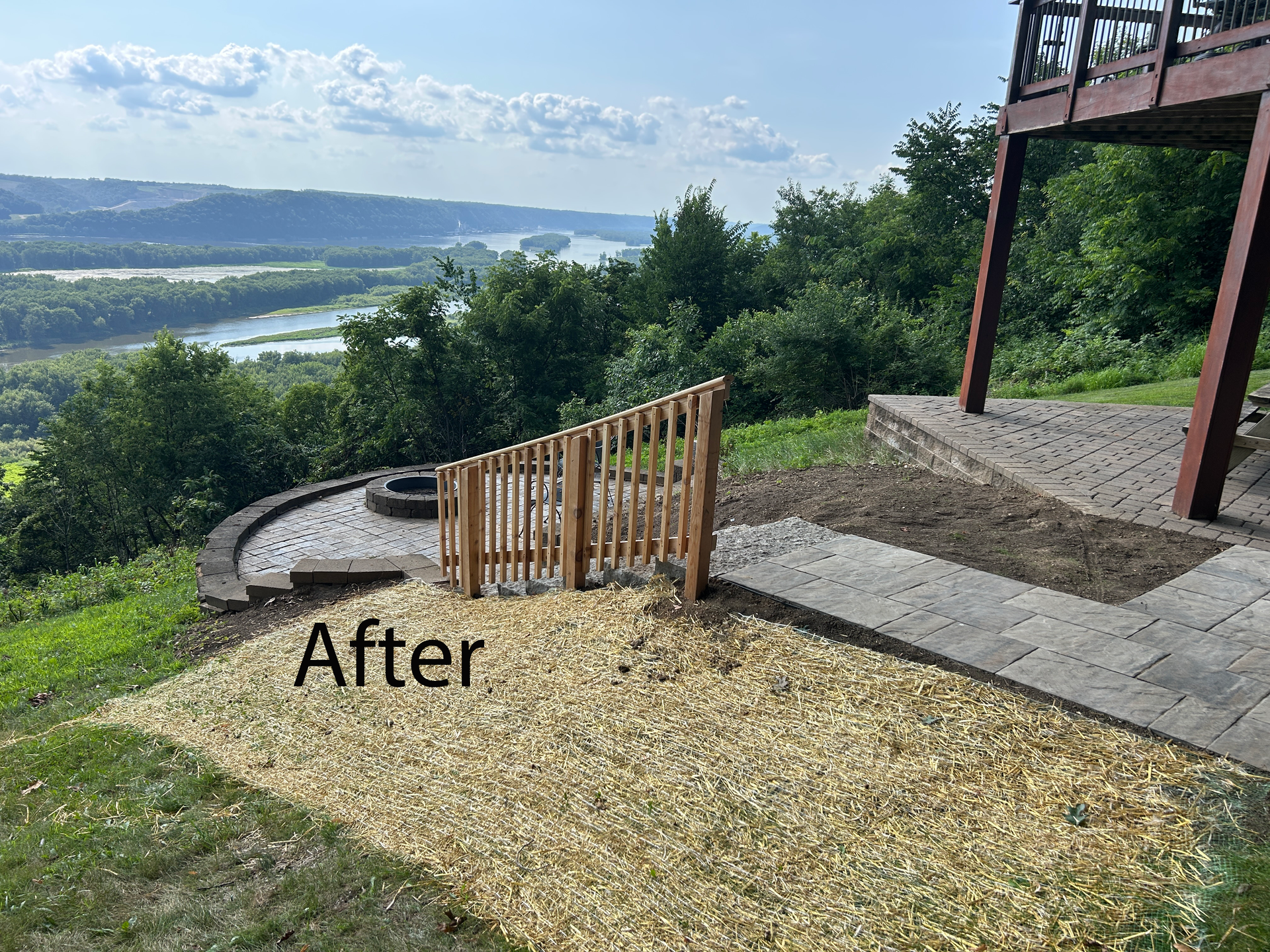 Terraced hillside garden with gravel path, wooden fence, and scenic valley view under blue sky