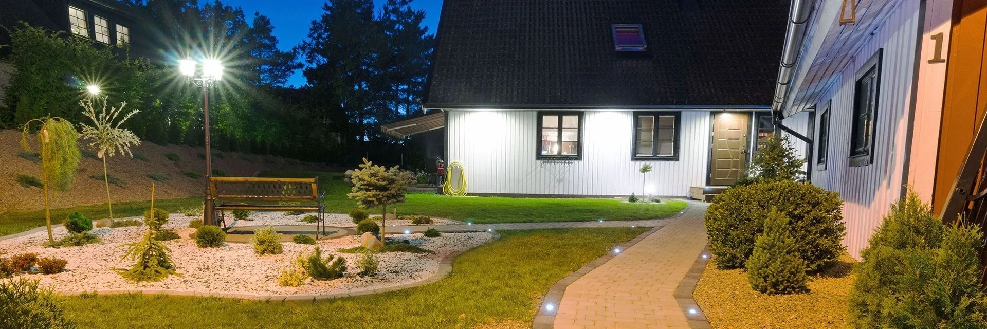 Night view of a house with a lit garden and pathway leading to the front door.
