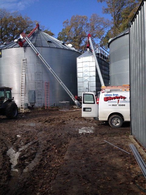 A white van is parked in front of a row of silos.