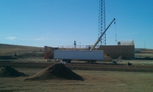 A white semi truck is parked in a dirt field with a crane in the background