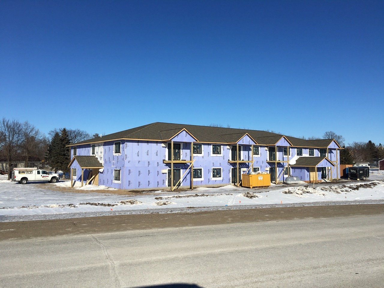A large purple building is being built next to a snowy road.