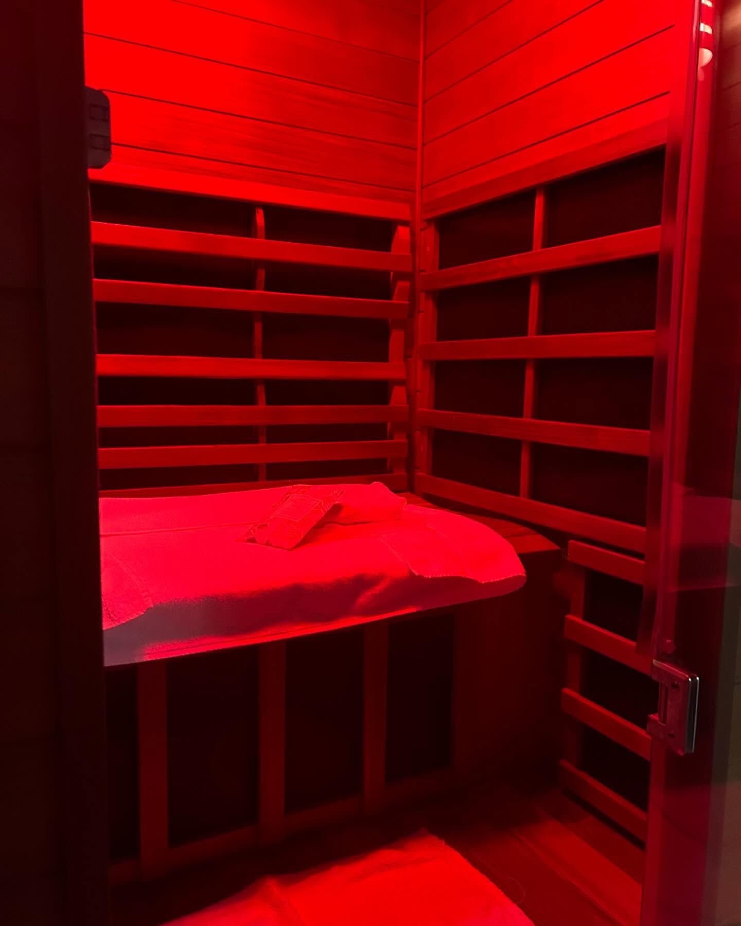 A sauna with red lights on the walls and a bed.