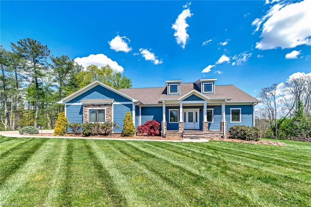 A blue one-story house with a dormer, front porch, and stone accents, situated behind a freshly mown, striped lawn.