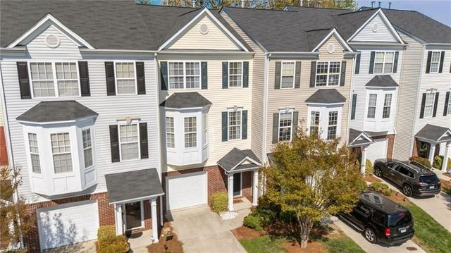 An aerial view of several attached three-story townhomes with grey roofs, light siding, and private garages.