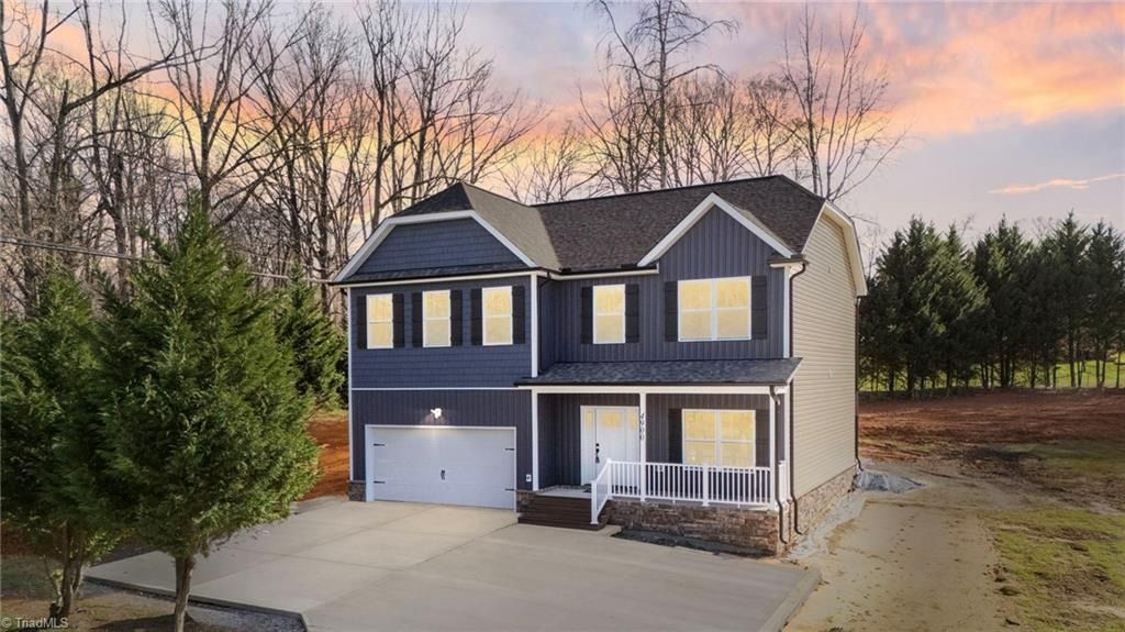 A two-story dark blue suburban house with a white garage, front porch, and concrete driveway at sunset.