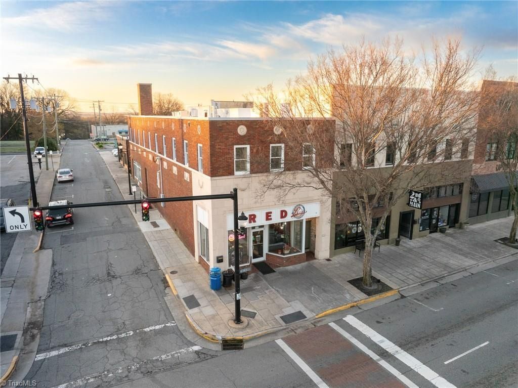 An aerial view of a brick commercial building on a street corner with shops, bare trees, and a crosswalk at sunset.