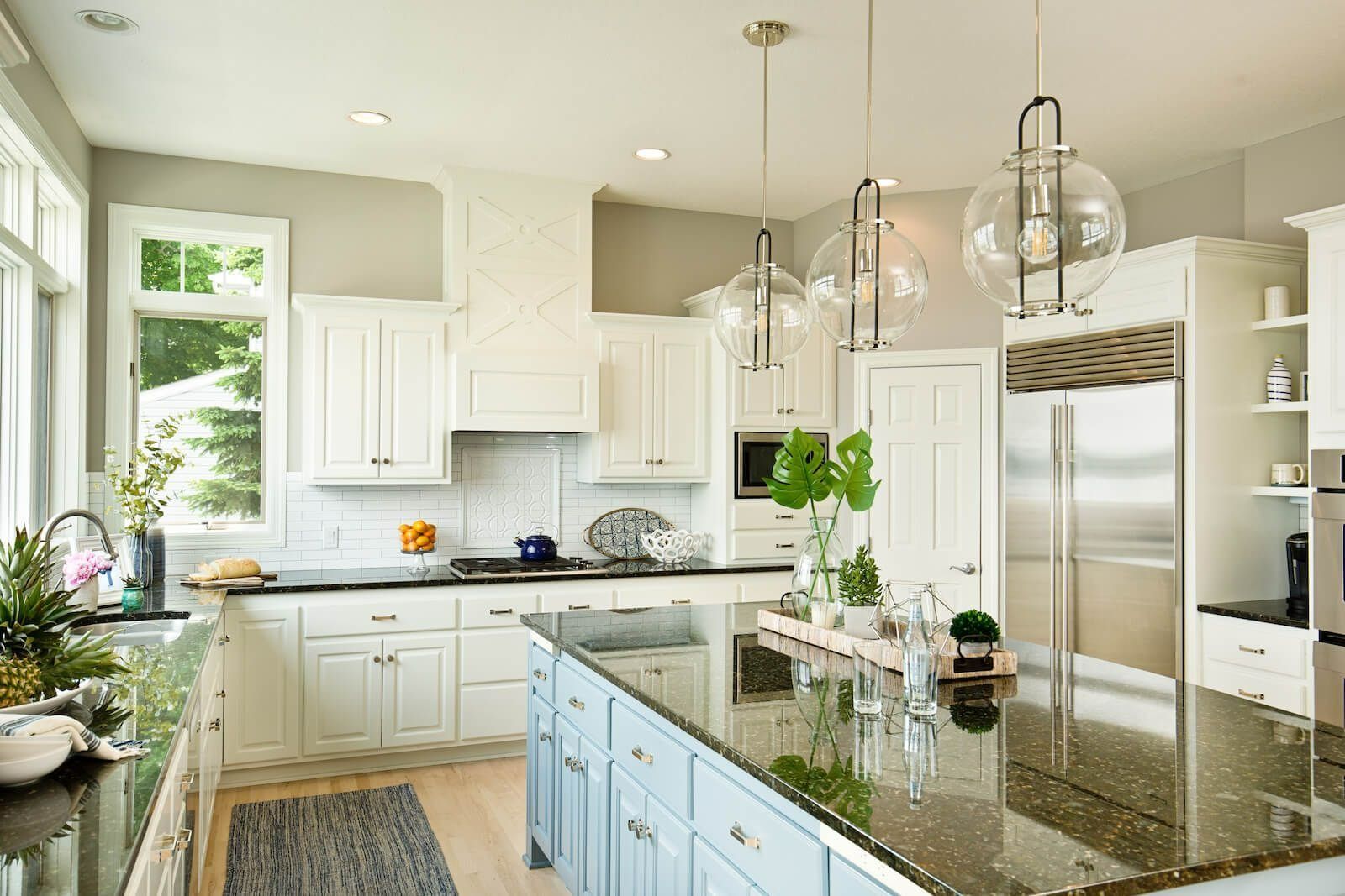 A bright kitchen with white cabinetry, a large central island, stainless steel refrigerator, and glass pendant lights.