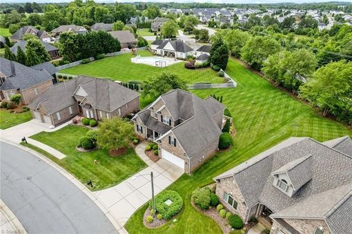 An aerial view of a suburban neighborhood featuring brick houses with grey roofs, green lawns, and a swimming pool.