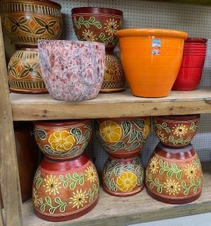 Decorative painted pots and planters stacked on wooden shelves, in red, orange, and floral patterns