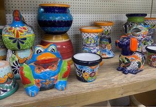 Colorful painted ceramic pots and figurines displayed on a wooden shelf, including a frog and owl designs