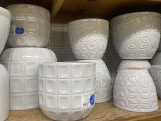 Stacked white ceramic plant pots with embossed patterns on a store shelf