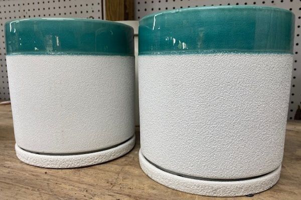 Two cylindrical white and turquoise planters on a wooden surface.