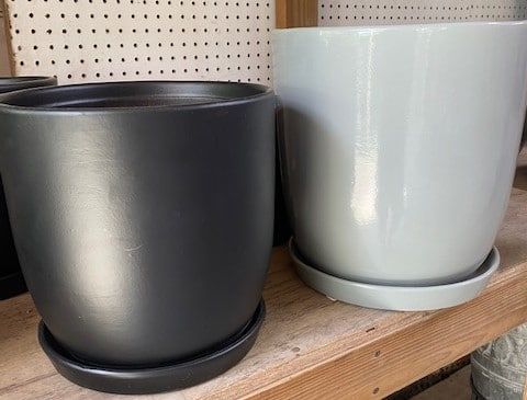 Two glossy ceramic flower pots, black and gray, with matching saucers on a wooden shelf.