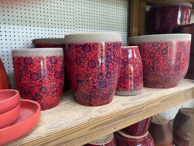 Red and purple floral glazed ceramic pots on a wooden shelf, various sizes and shapes, neutral rim.