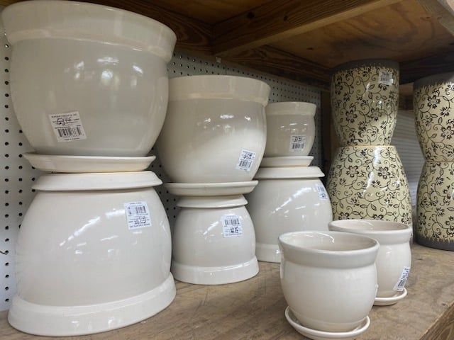 White ceramic flower pots on a wooden shelf, some with saucers.