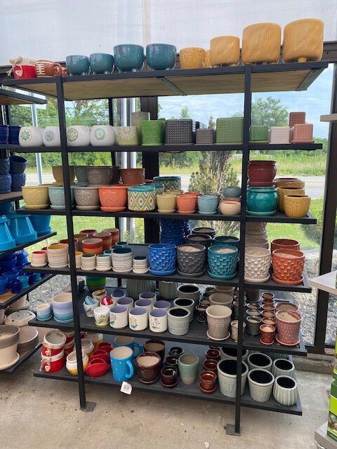 Shelves displaying a variety of colorful ceramic plant pots in an outdoor setting.