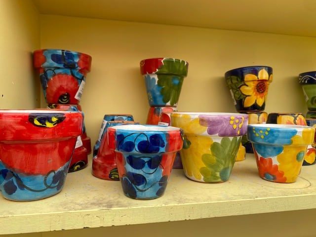 Colorful, hand-painted ceramic flower pots on a shelf. Designs include flowers and abstract patterns in various colors.