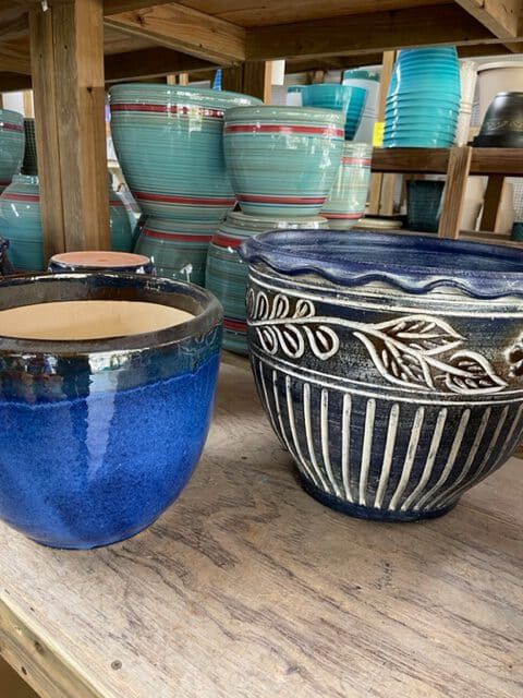 Close-up of blue ceramic planters in various shapes and sizes, displayed on wooden shelves.