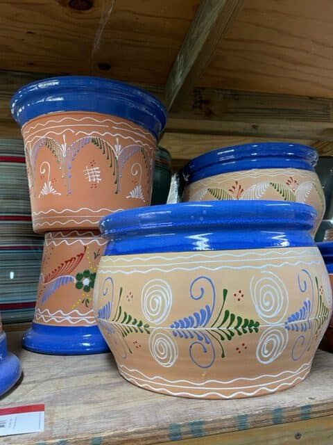 Earthenware pots with blue rims and painted floral designs, stacked on a wooden shelf.