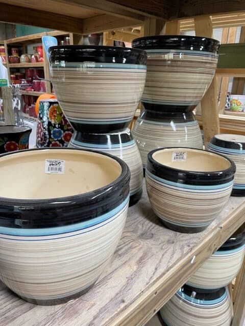 Planter pots with striped patterns and black rims on a wooden shelf.