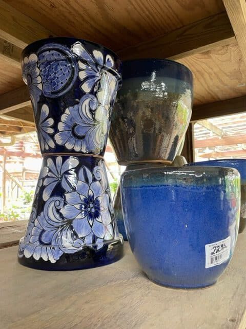 Blue ceramic pots in a garden center: floral pattern, glazed, stacked on wooden shelf.