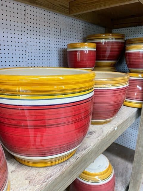 Red and yellow ceramic flower pots arranged on a wooden shelf.