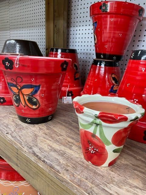 Red and painted flower pots on a wooden shelf. One has a butterfly design, another with red flowers.