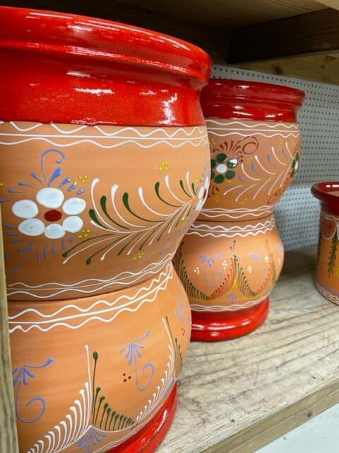 Terra cotta pots with red rims, decorated with floral patterns, stacked on a wooden shelf.
