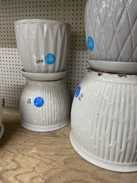 White ceramic planters stacked on a wooden shelf, displayed inside a store.