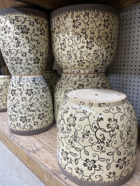 Ceramic planters with floral pattern, stacked on a wooden shelf. Cream and brown tones.