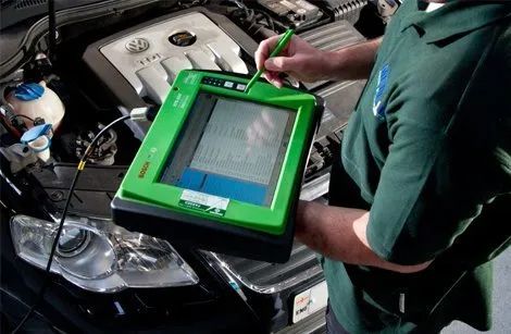 A man in a green shirt is using a tablet under the hood of a car.