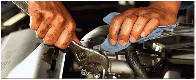 A person is working on a car engine with a wrench and a cloth.