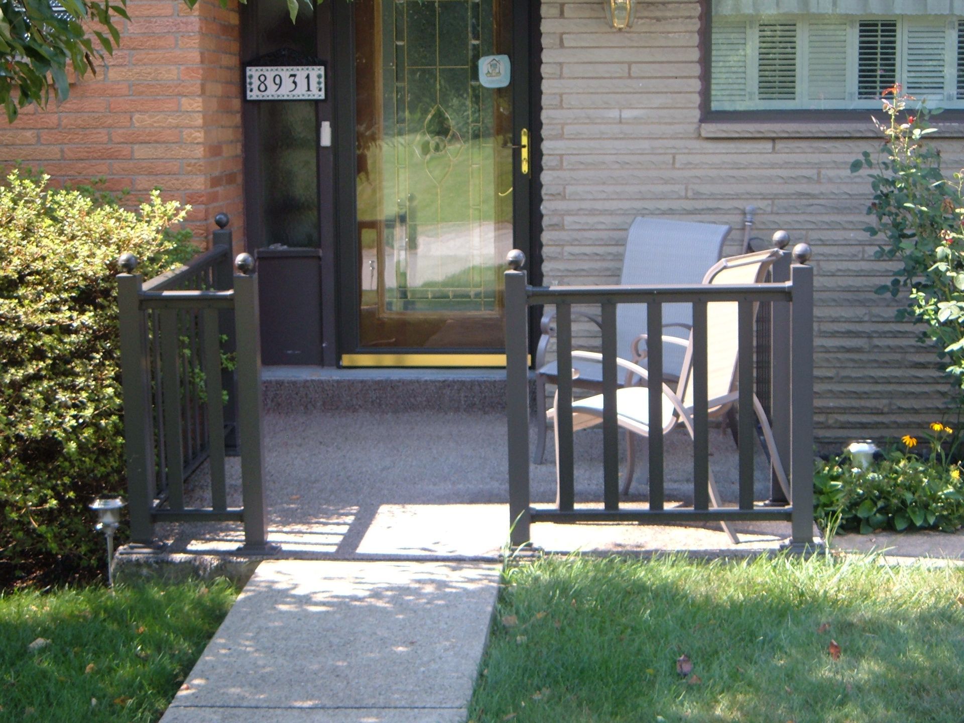 Front walkway to a townhouse entrance with black railing, chair, and glass door.