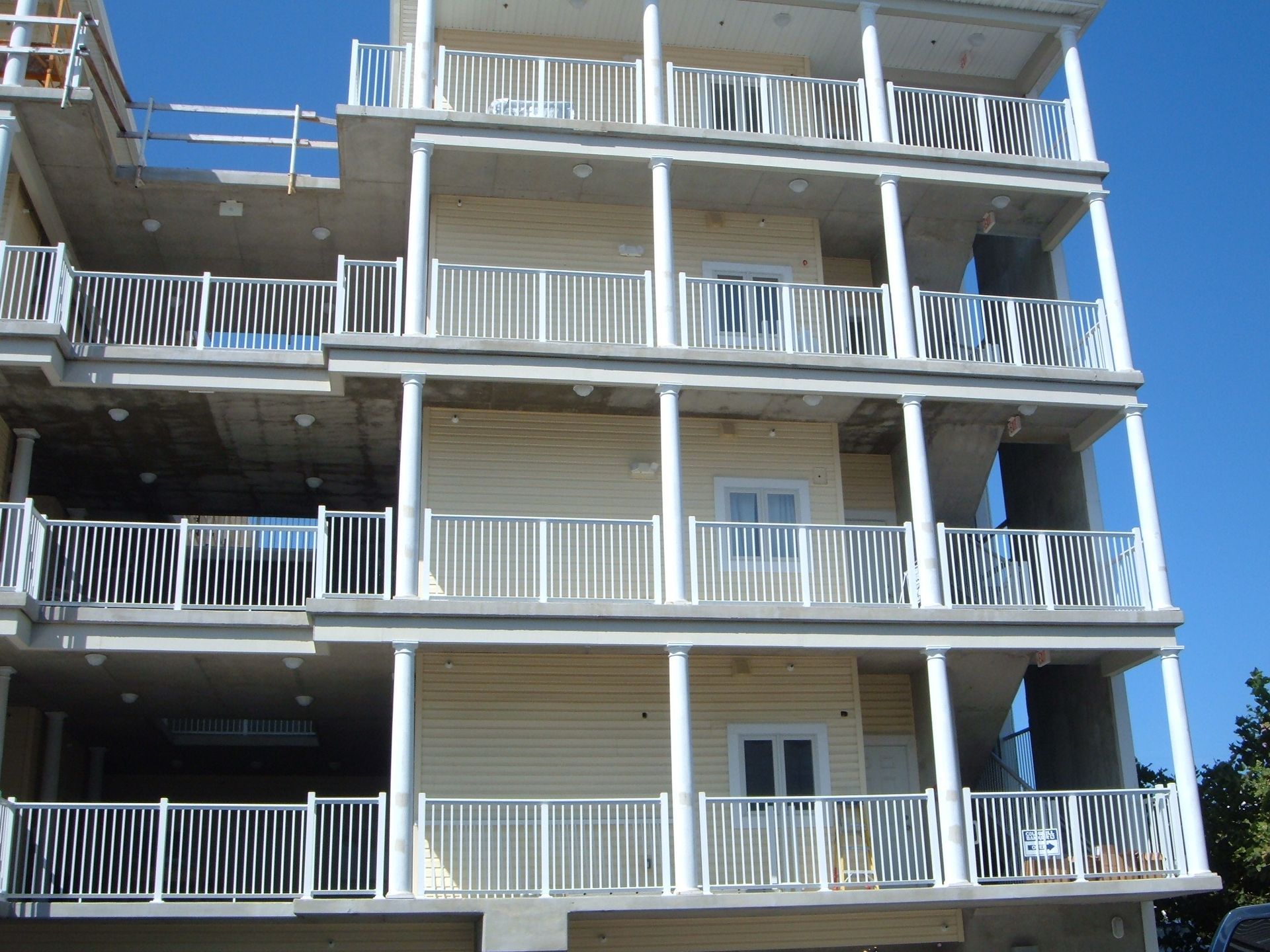 Multi-story apartment building with white balconies and beige siding under a clear blue sky