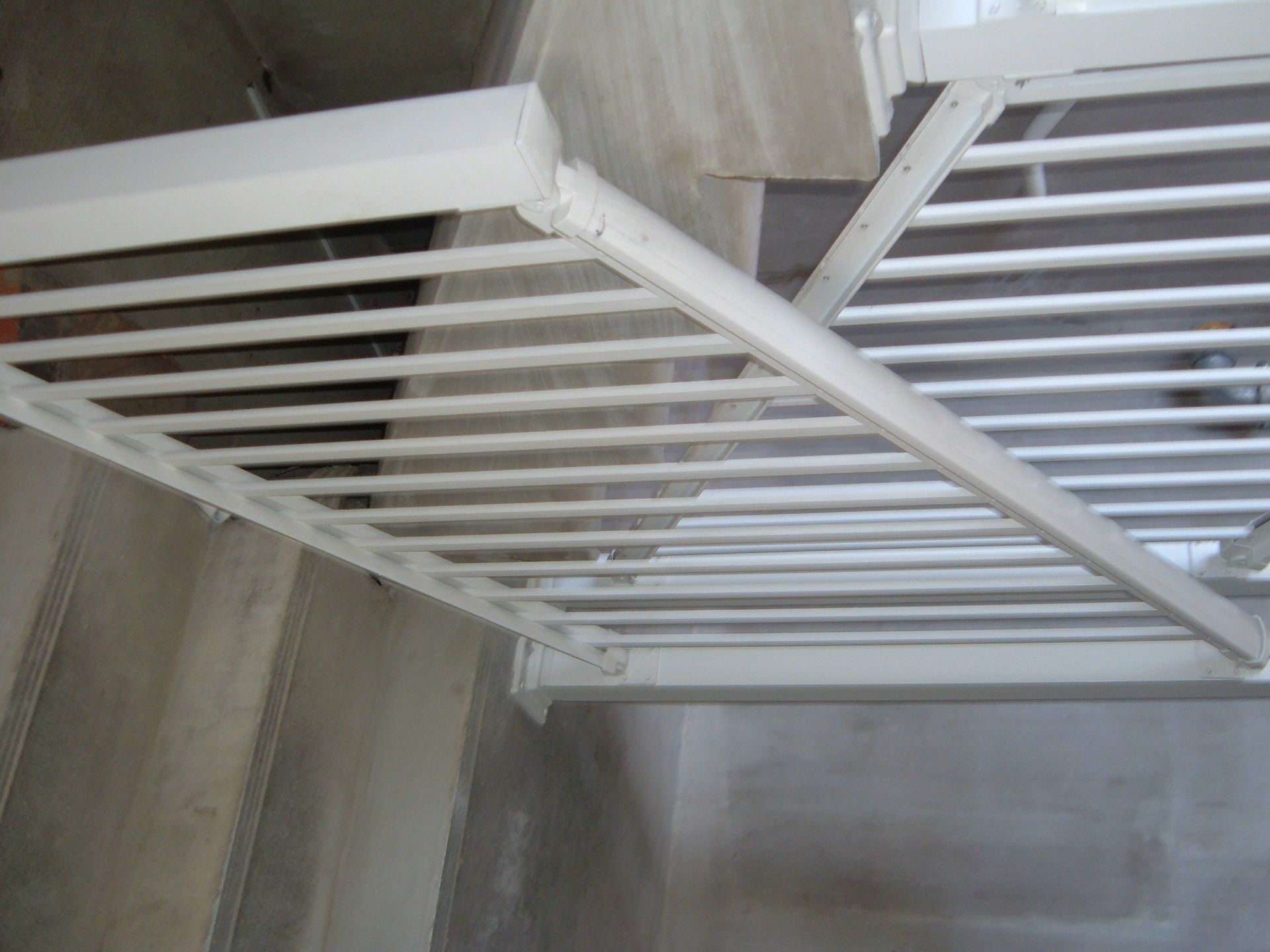 White metal clothes-drying rack mounted on a concrete wall indoors