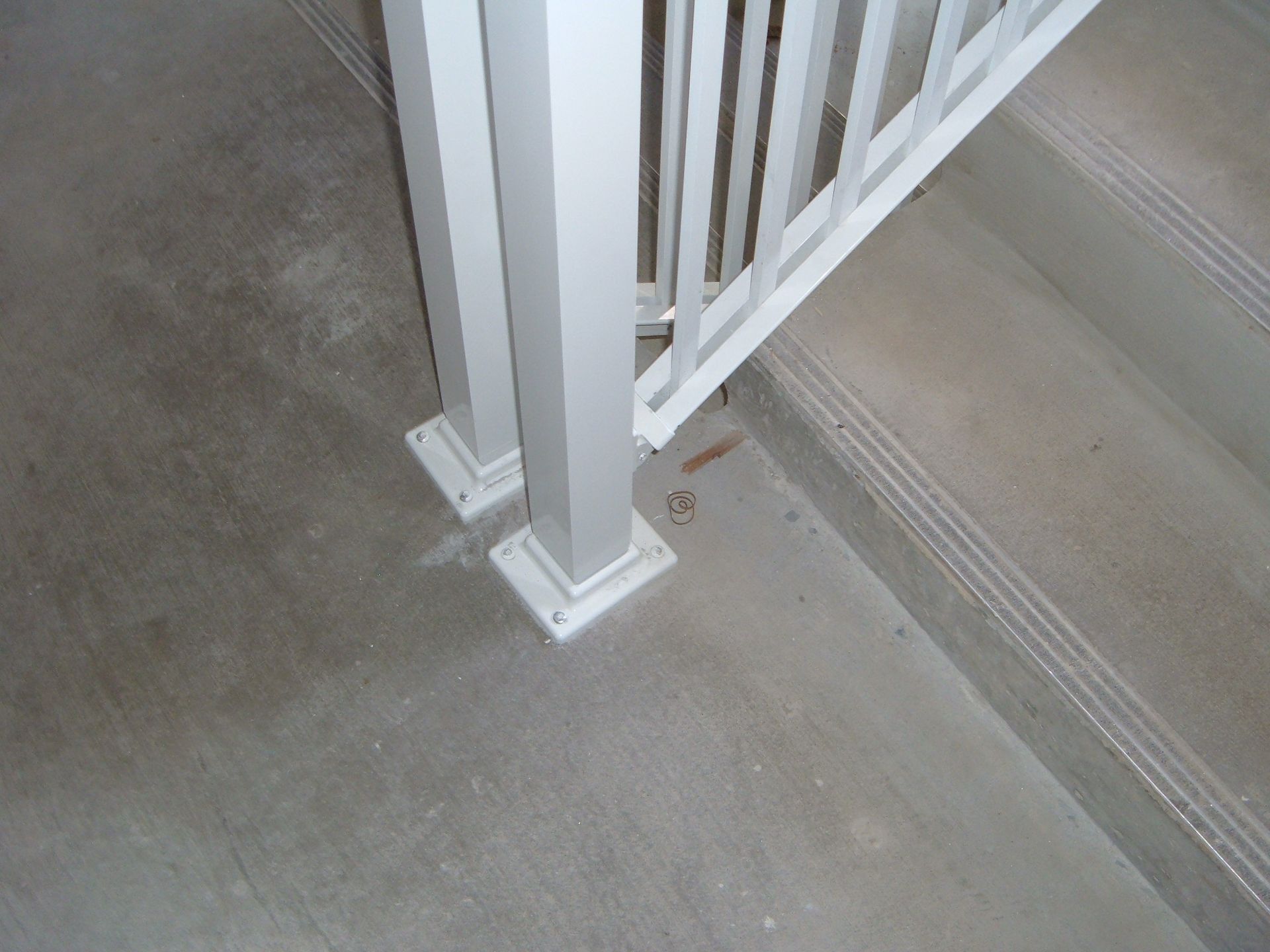 White stair railing post bolted to a concrete floor beside carpeted steps