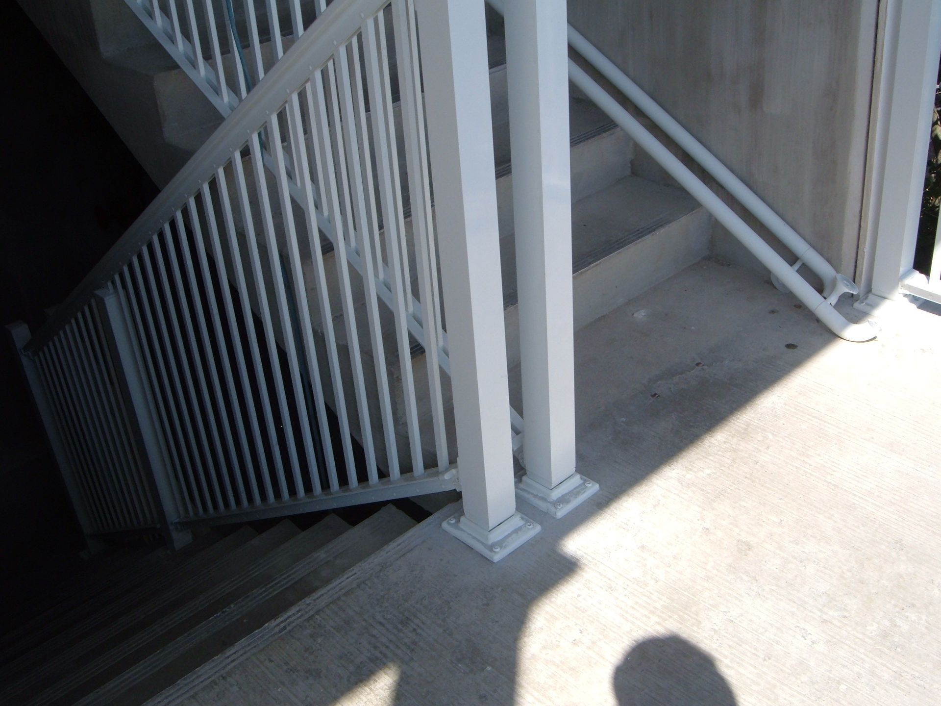 Concrete stairwell with white metal railings and bright sunlight on the landing