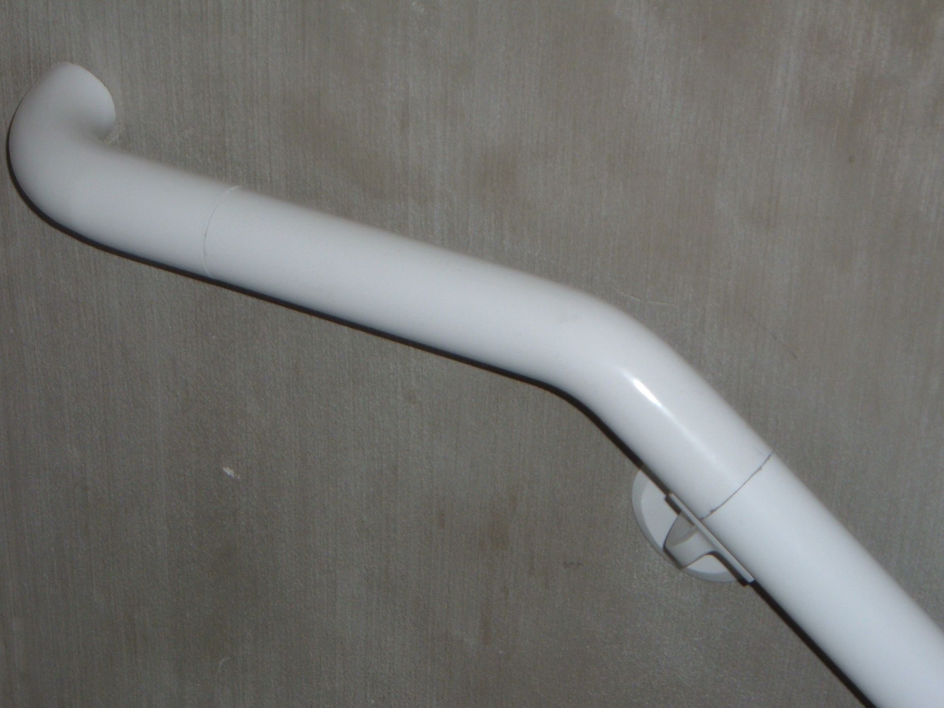 White curved grab bar mounted on a beige wall