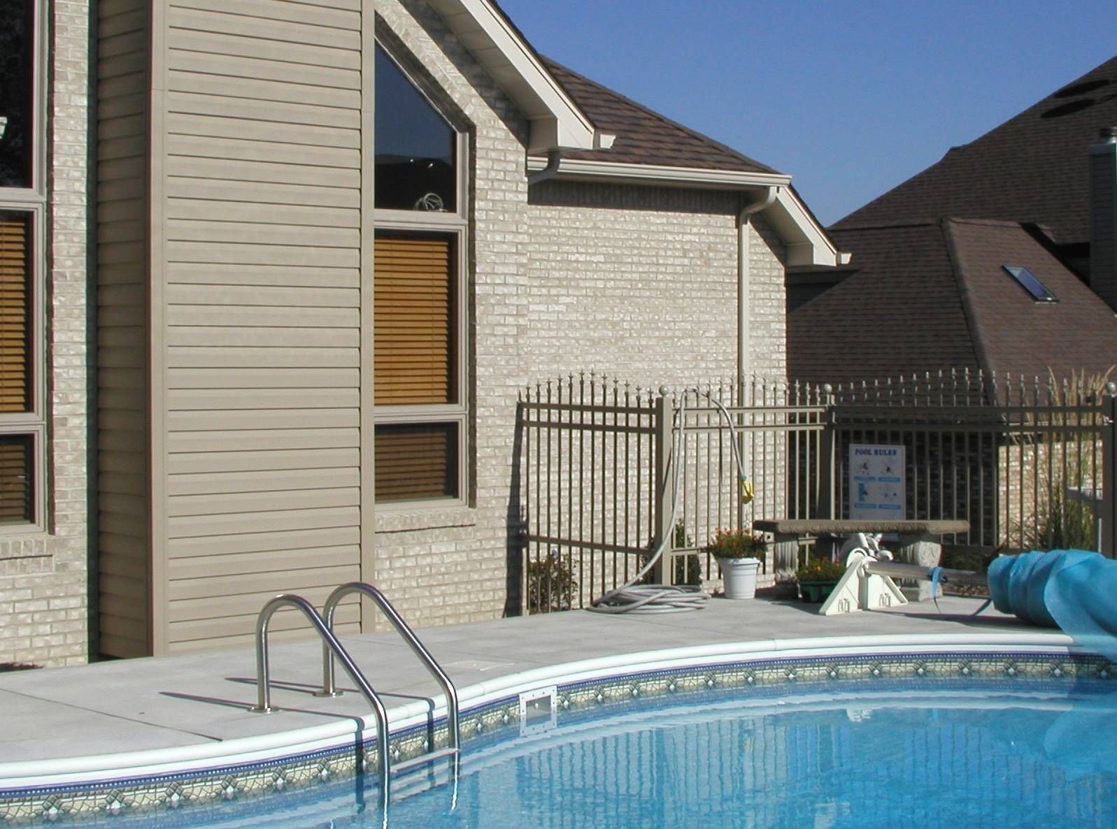 Swimming pool beside a modern house and fenced patio on a sunny day
