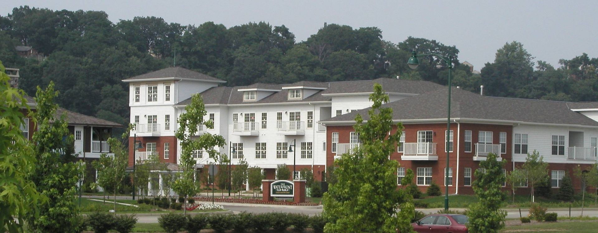 Apartment complex with red brick and white buildings beside a tree-lined road