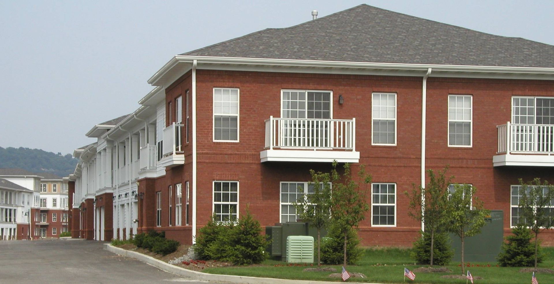 Red brick apartment building with white balconies and windows along a quiet street