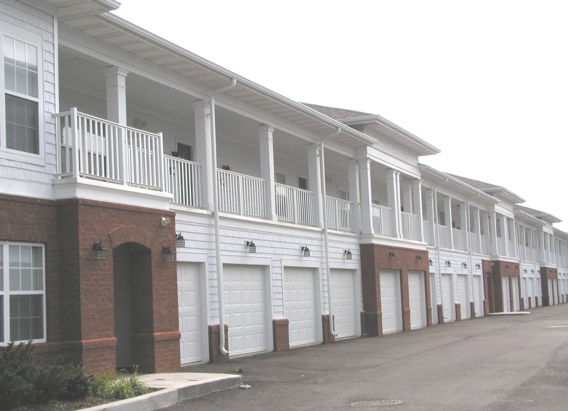 Row of white townhouses with brick facades and garages along a paved street