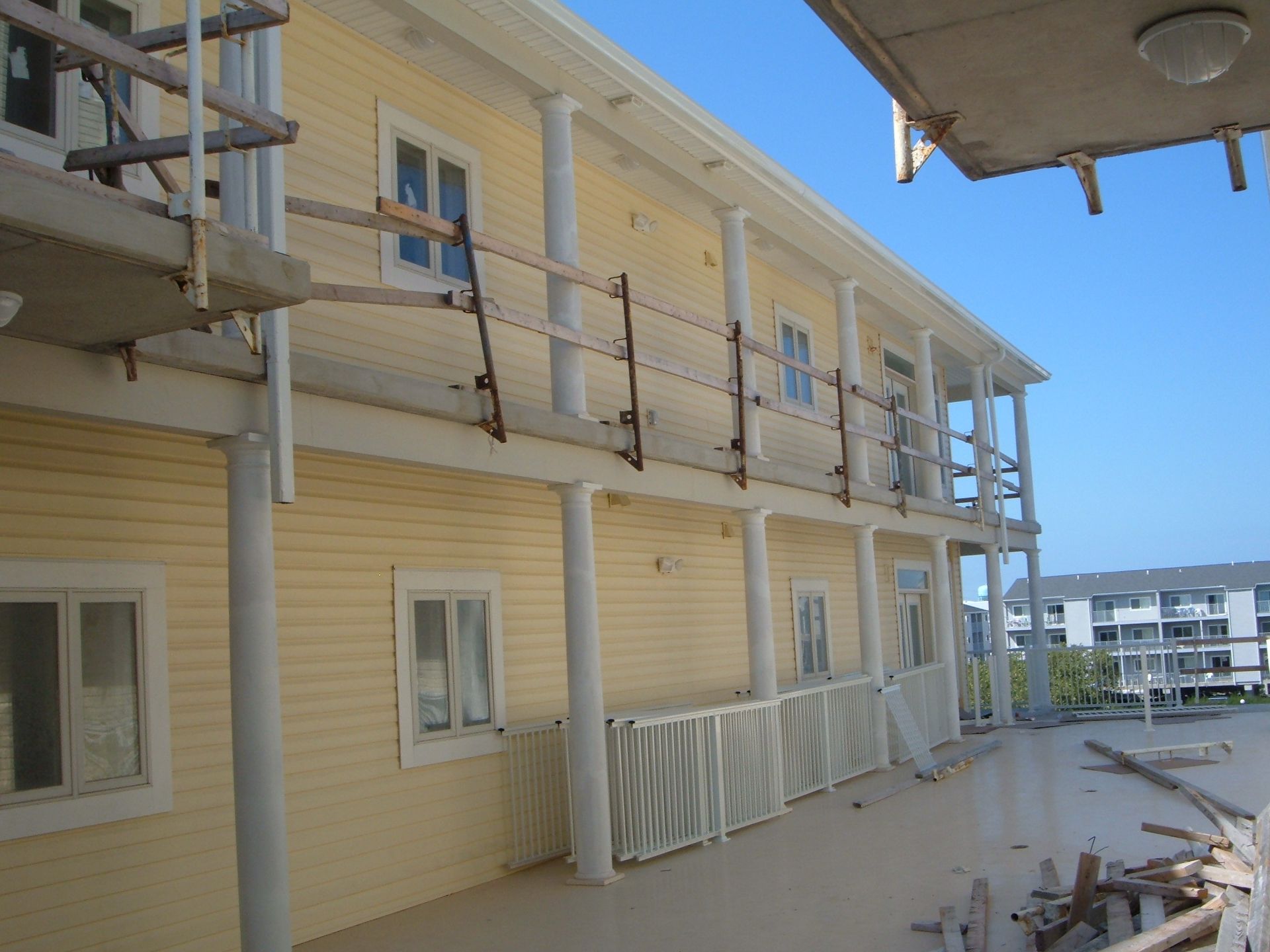 Yellow two-story building with metal balconies and railings on a construction site under a blue sky