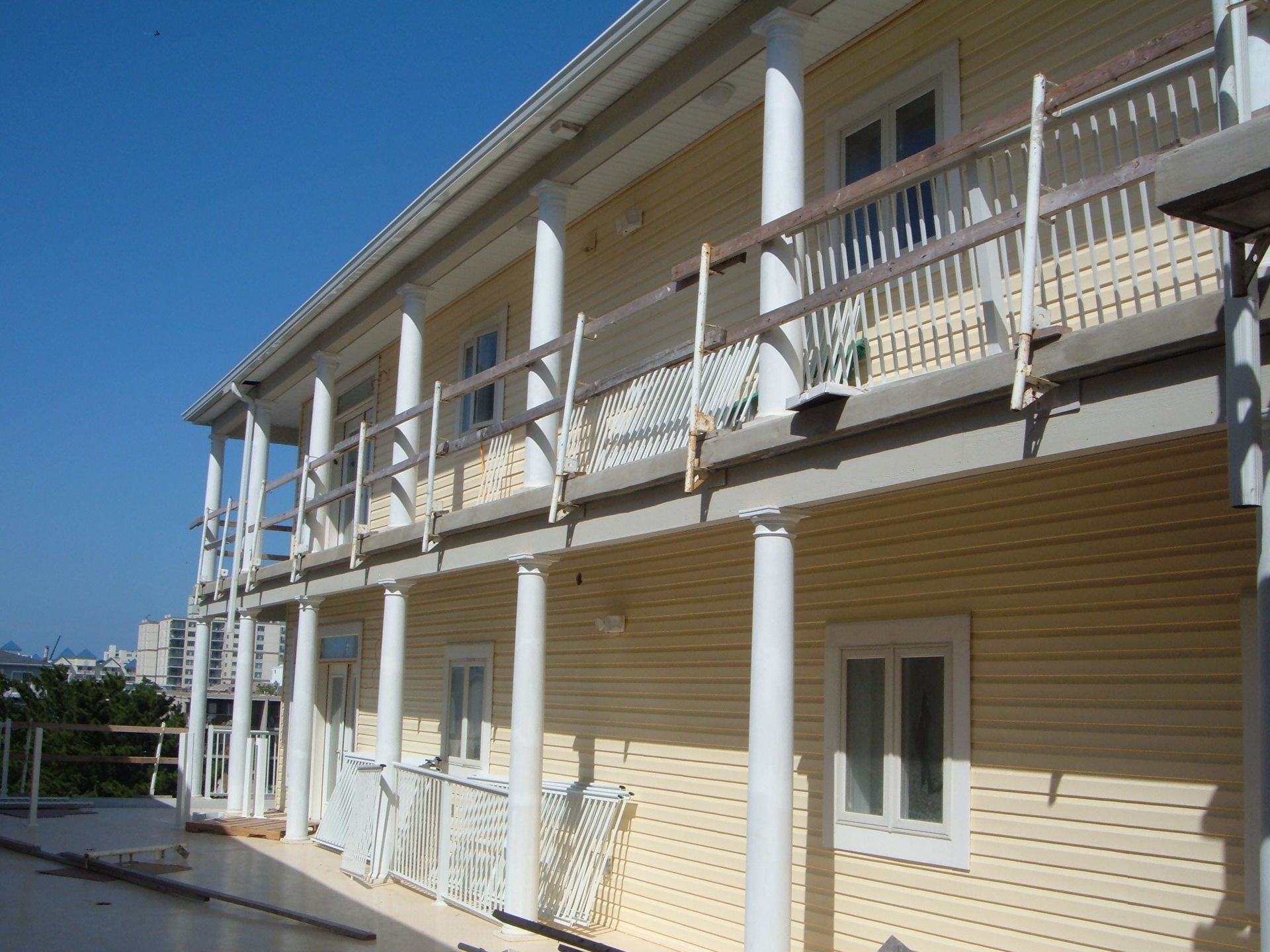 Two-story beige building with white columns, balconies, and windows under a clear blue sky