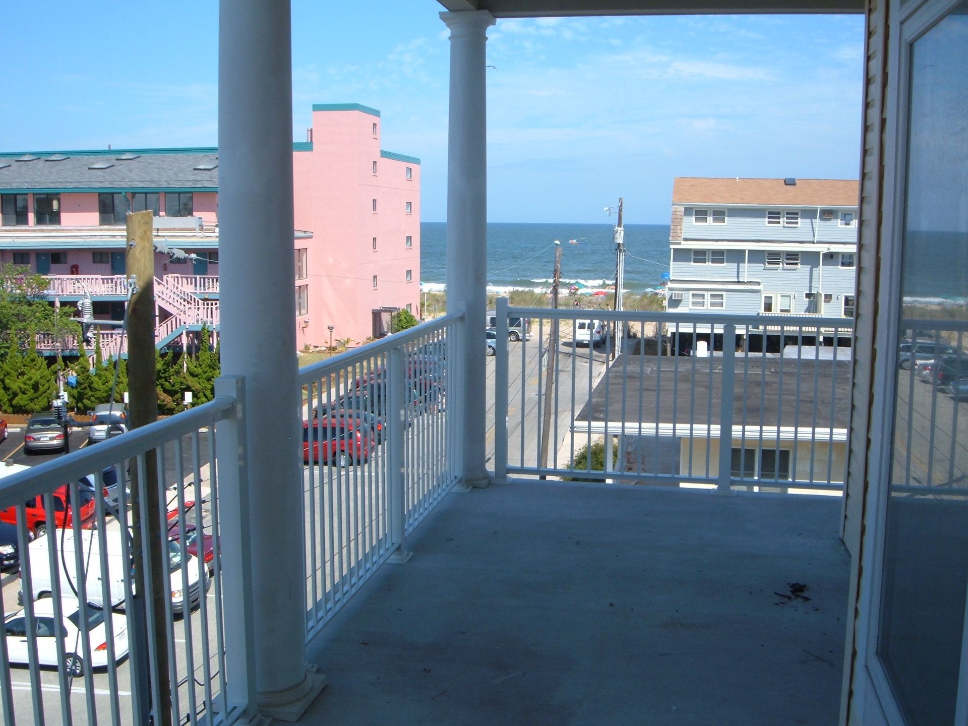 Balcony overlooking seaside street, with pink and white buildings and ocean in the distance