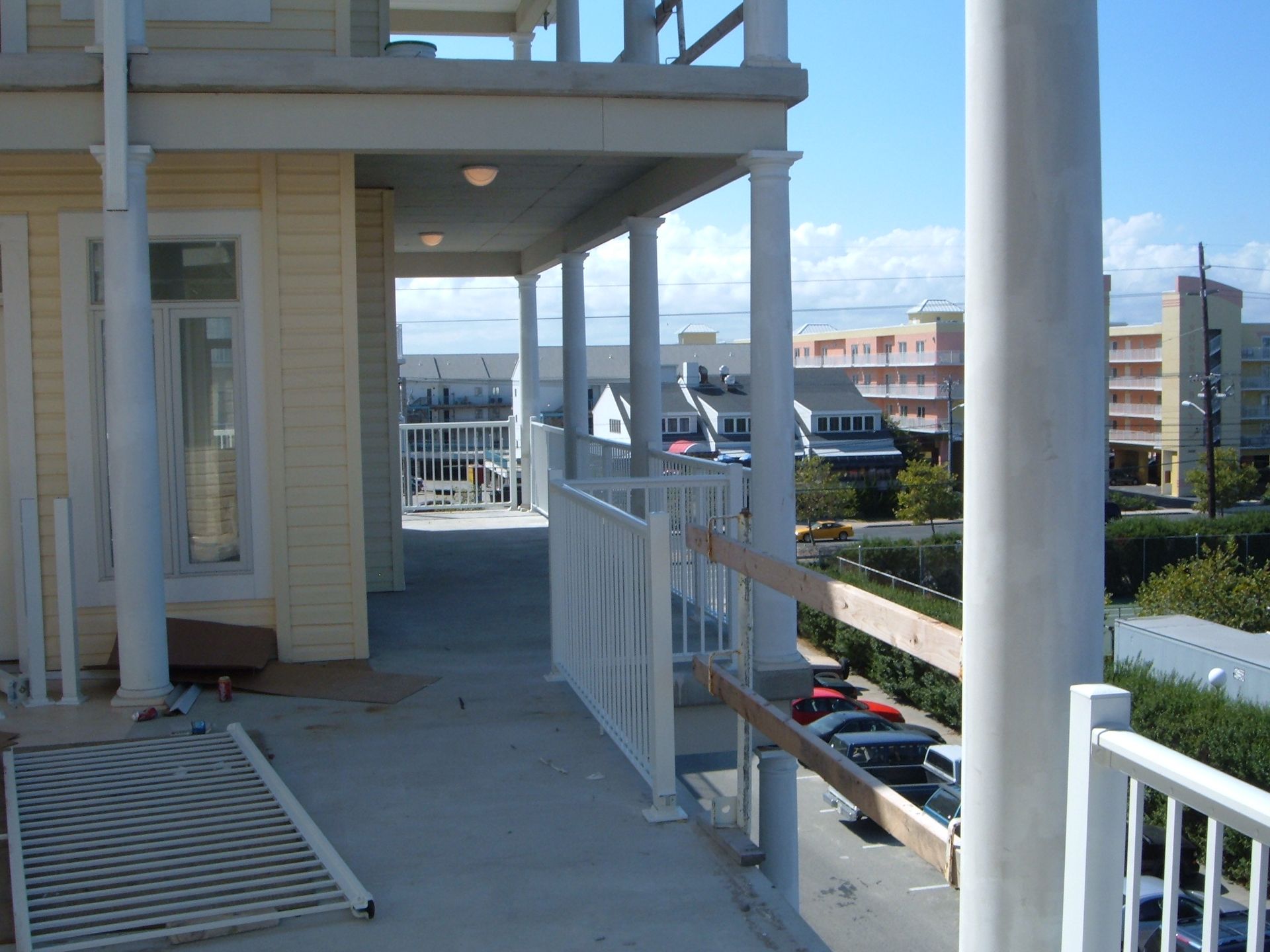 Balcony walkway beside a beige building, with white railings and parked cars below overlooking the waterfront.
