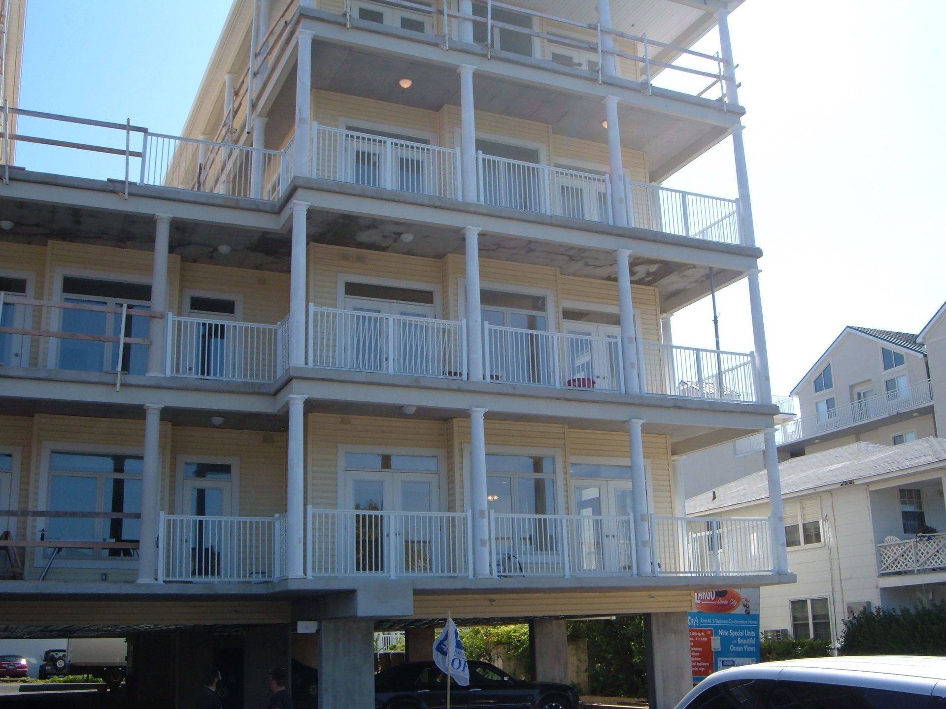 Multi-story beige apartment building with white balconies and railings on a sunny street