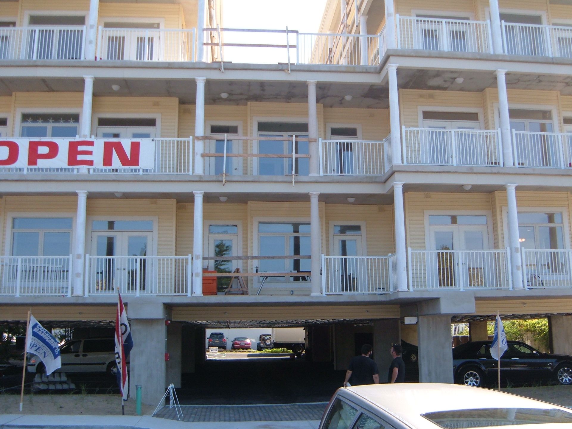 White multi-story building with balconies, an open sign, and parked cars underneath.