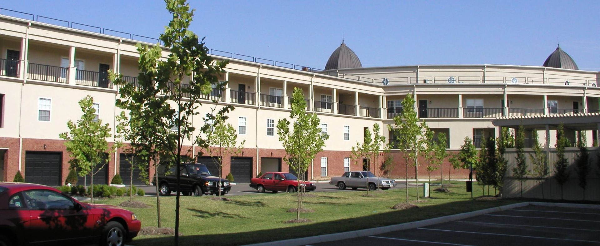 Modern apartment complex with balconies, red cars, trees, and a covered walkway in front